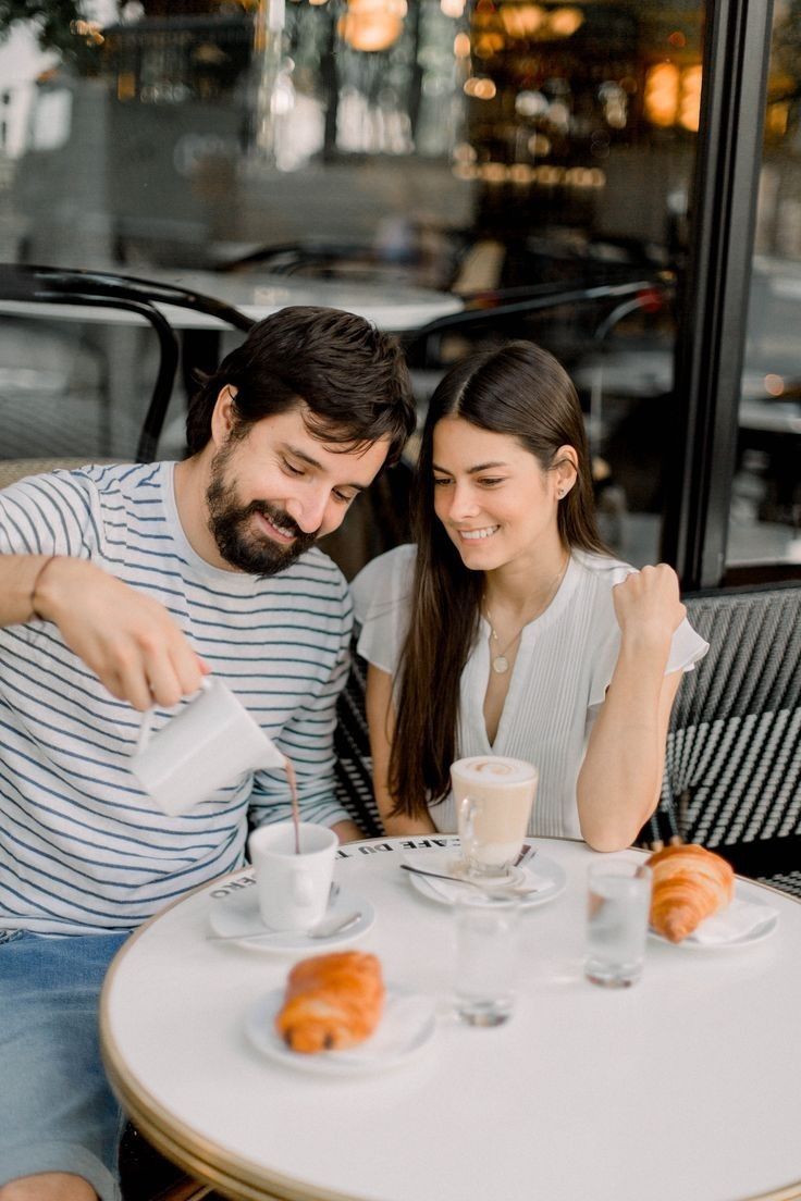 This may contain: a man and woman sitting at a table with doughnuts
