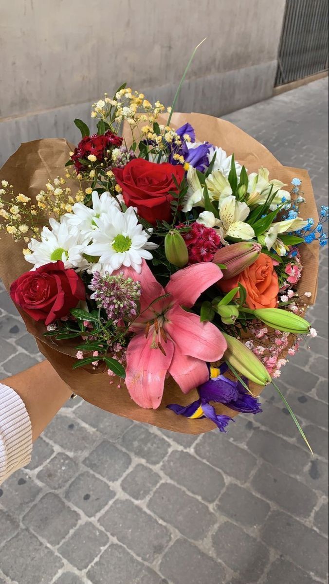 This may contain: a person holding a bouquet of flowers in their hand on the street with brick pavement